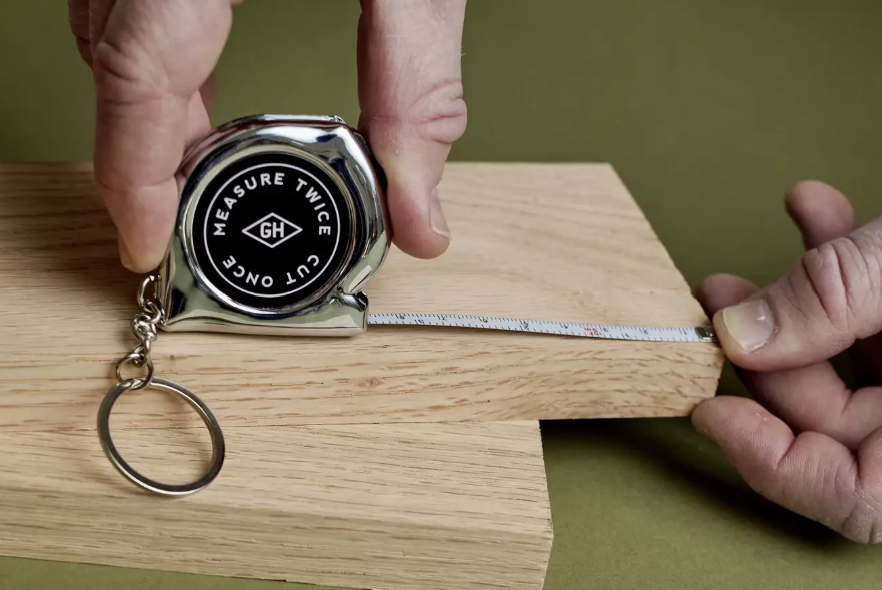 Person using a tape measure on a wooden block with a green background